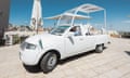 A man sits in the driver's seat of the white popemobile