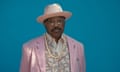 older man wearing a pink suit and matching hat looks ahead