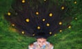 A woman lies on the grass, her long, black hair spread out and dotted with little yellow flowers