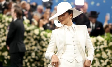 person wearing white hat, suit and pants looks down