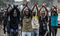 Protesters make X signs with their arms. Those who are identifiable are young men