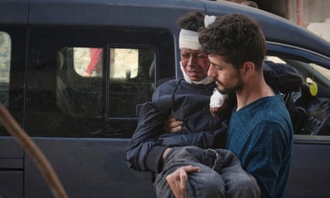 A boy grimacing in pain with a bandage on his head being carried into hospital by a man