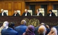 Five judges seated on ivory coloured seats with the backs of heads of onlookers below
