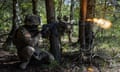A soldier fires a rifle in woodland.